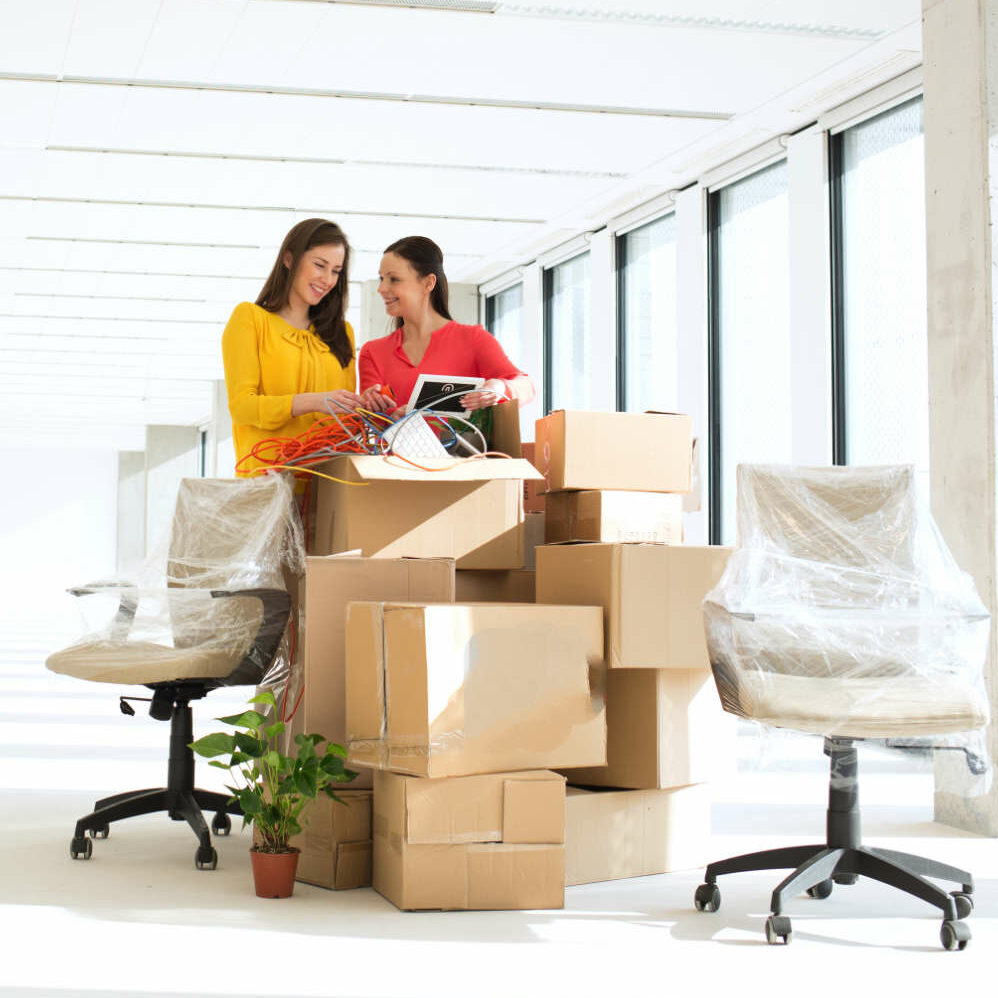 Businesswomen unpacking cardboard boxes in new office